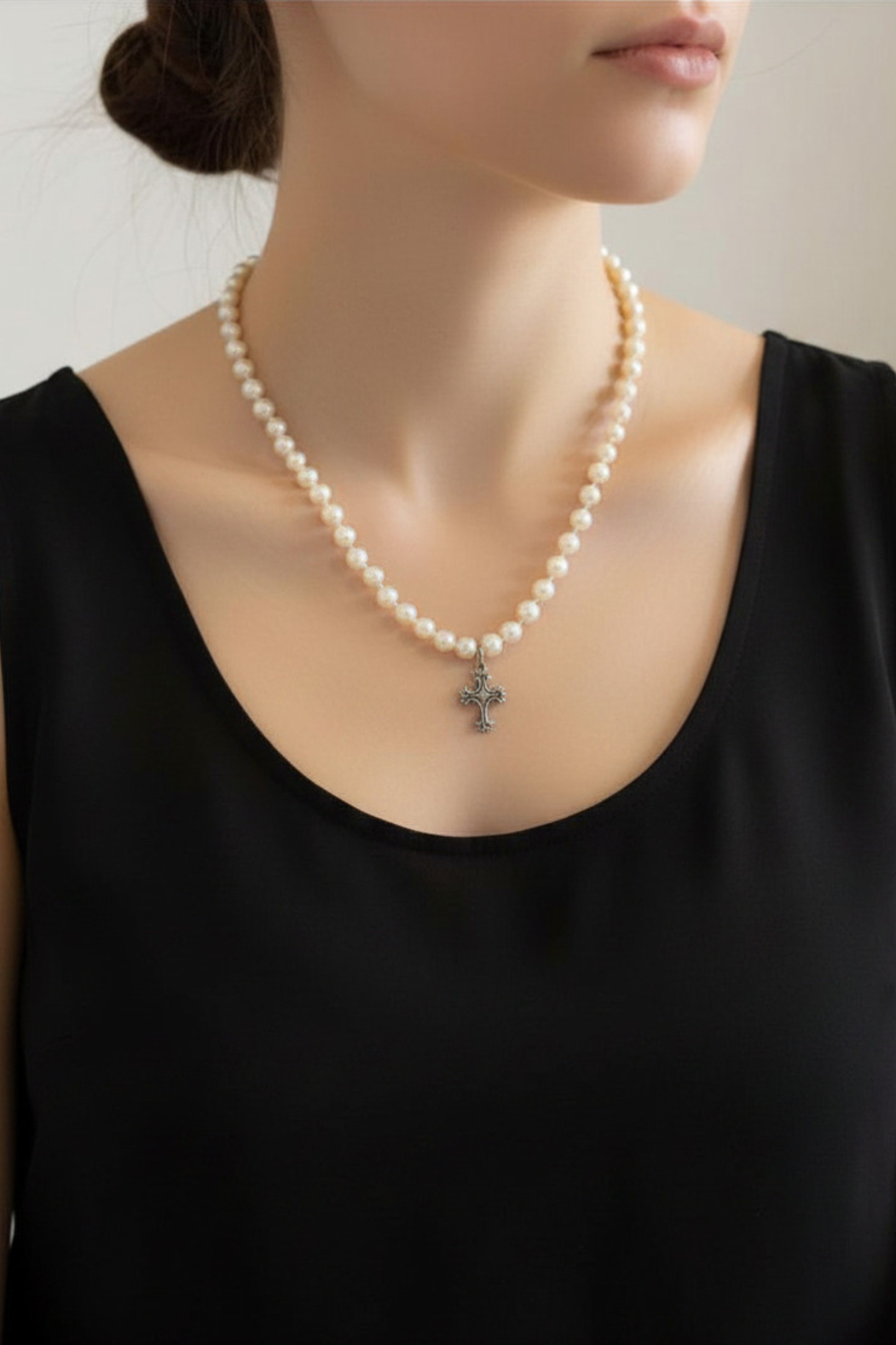 Pearl necklace with a cross pendant worn by a person in a black top.