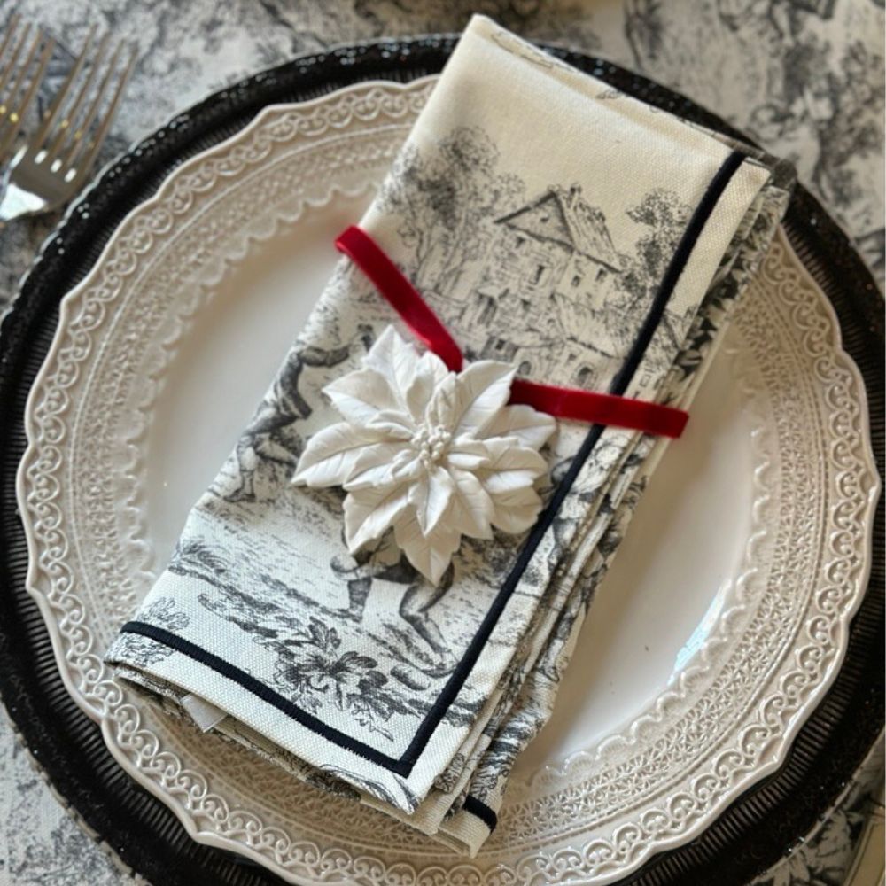 Decorative black & Cream toile folded napkin with a porcelain white poinsettia flower on a Finezza plate