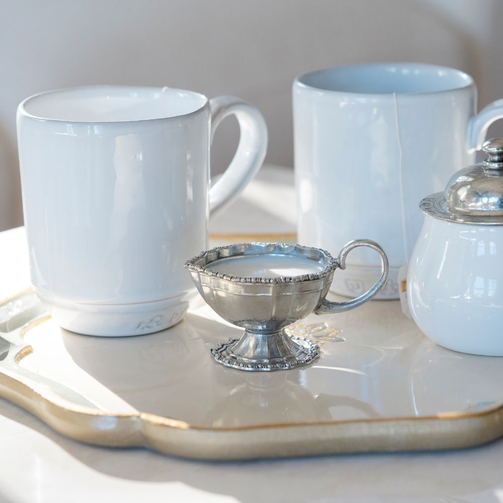 Pewter creamer styled on tray with white coffee mugs.