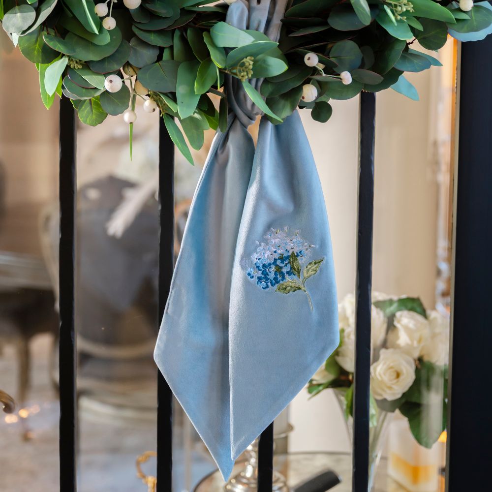Light blue sash with floral embroidery hanging on a decorative wreath.