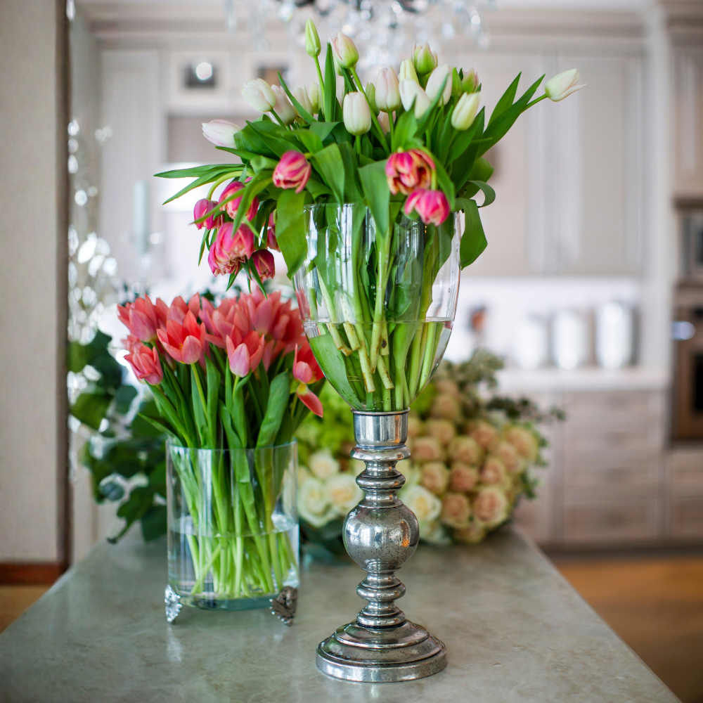 Giovanna large fluted hurricane with pewter base and glass bowl, filled with pink tulips on a counter with other flowers