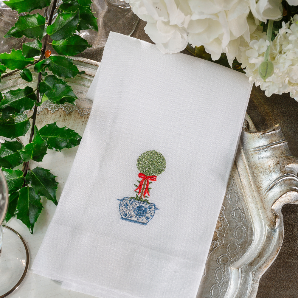 A white linen towel embroidered with a La Jardin topiary on a Silver tray with holly and white flowers