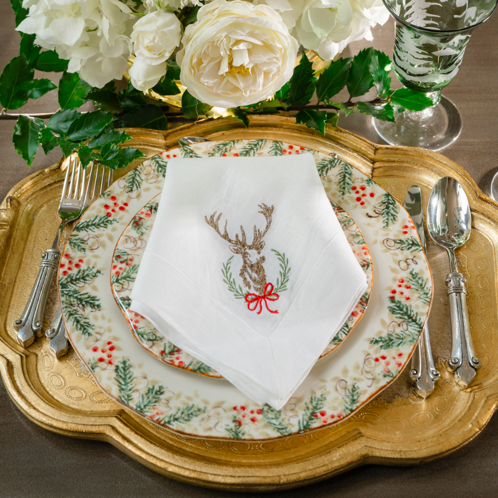 A Laurel Wreath Stag with Bow Large White embroidered Linen Napkin folded on a Natale Dinner plate on a gold Florentino Tray