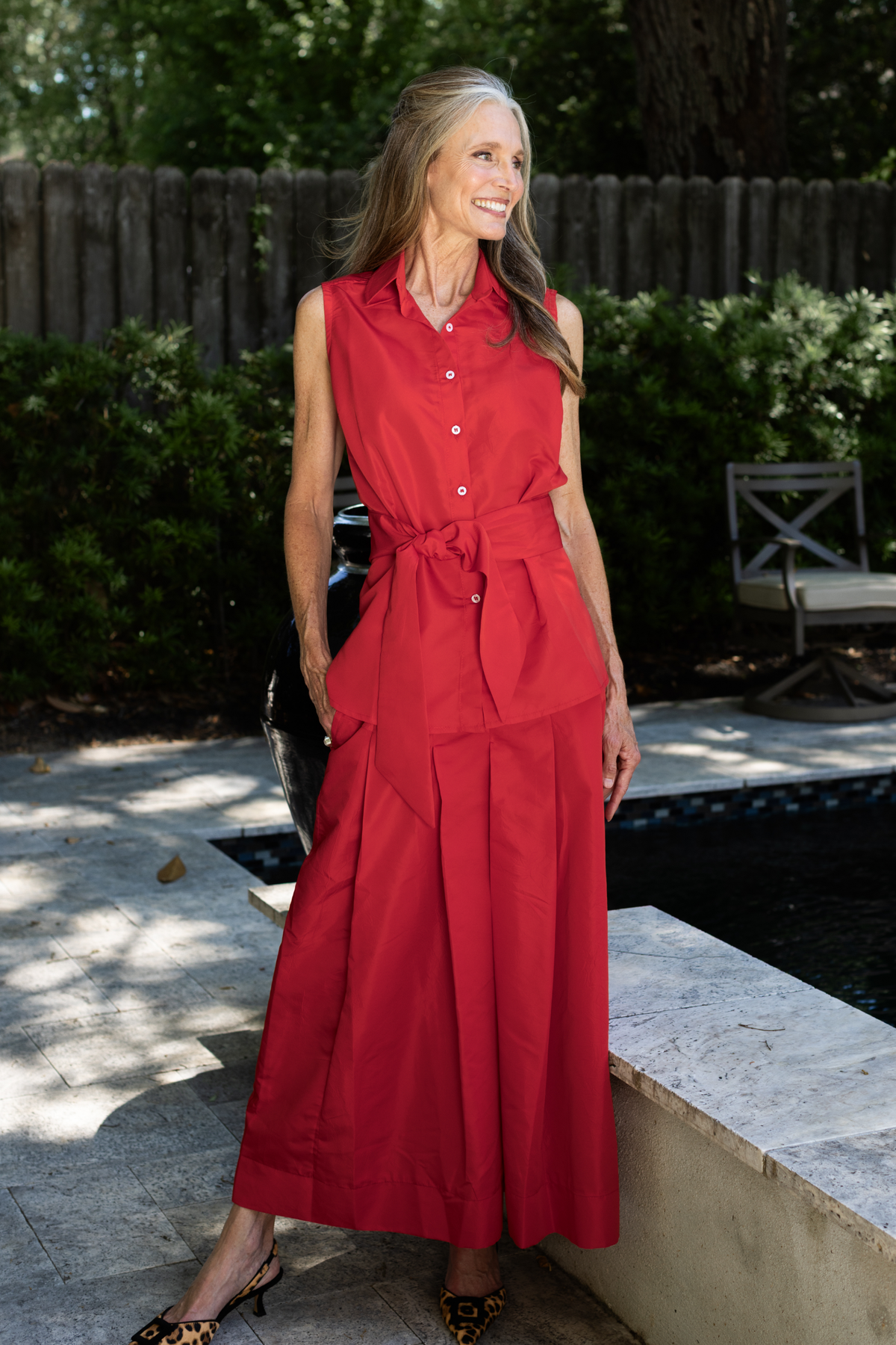 A woman standing by a pool wearing a Lizzy taffeta skirt with a Caroline sleeveless top with a sash
