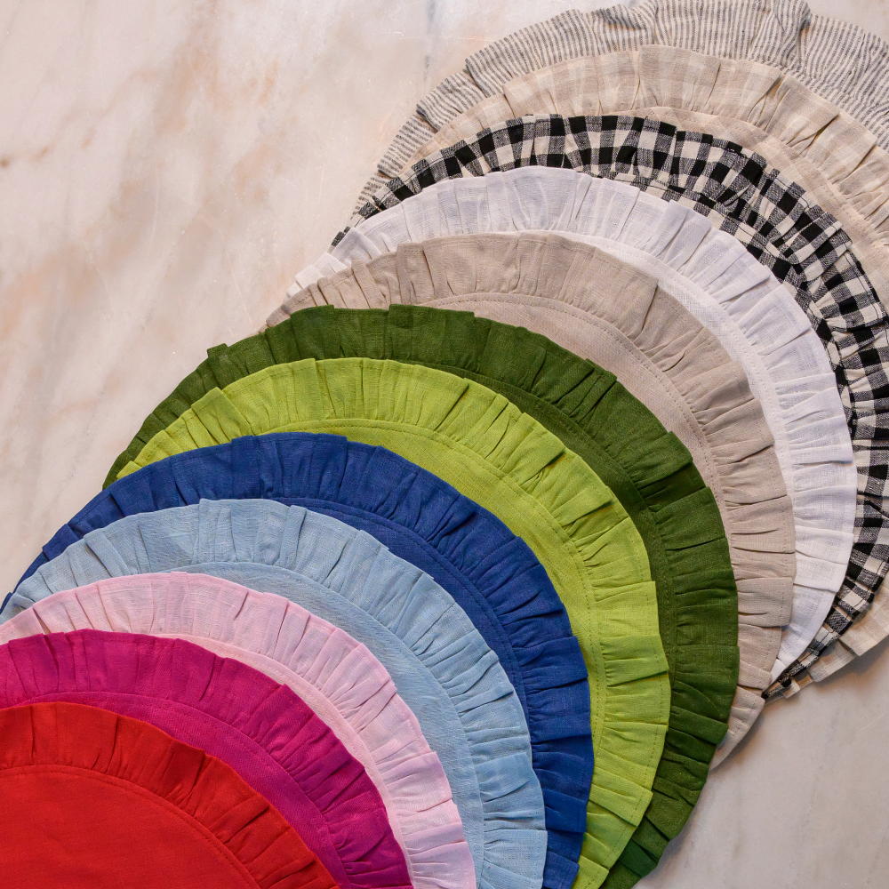 Various colors offered or round ruffle linen placemat lined up on table.
