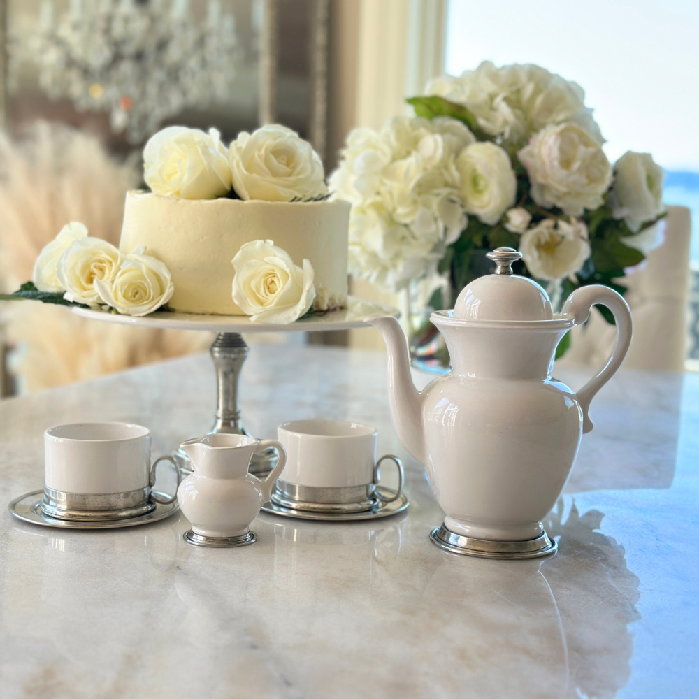 Tea set and cake with white flowers on a marble surface.