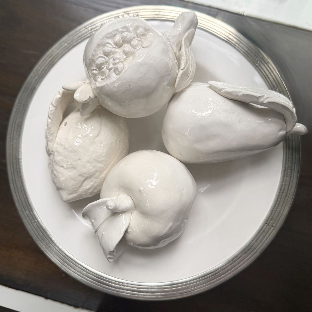 White ceramic fruits on a Tuscan plate with a dark background
