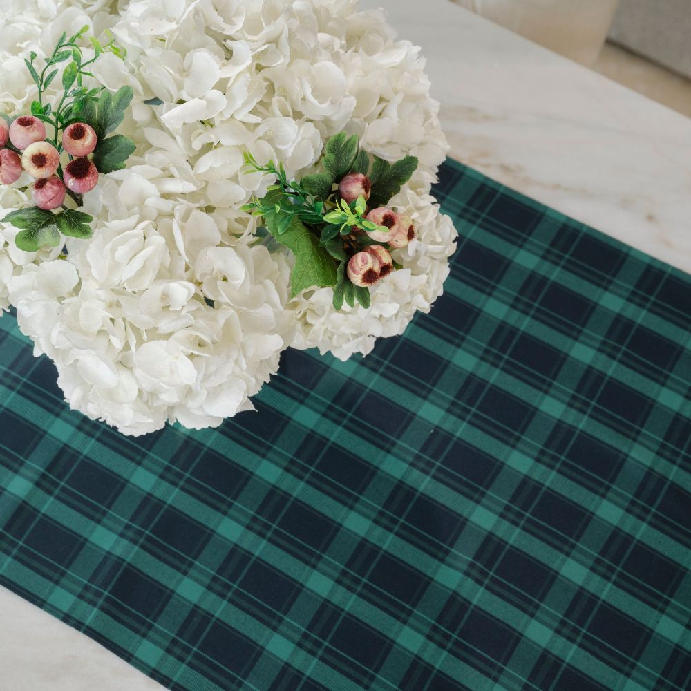 White flowers with green leaves and pink buds on a green plaid tablecloth.