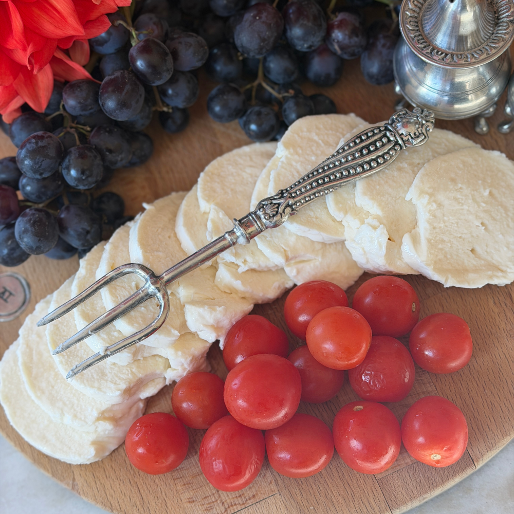 A Tavola pewter bread fork on a wooden cheese board with mozzarella tomatoes and grapes