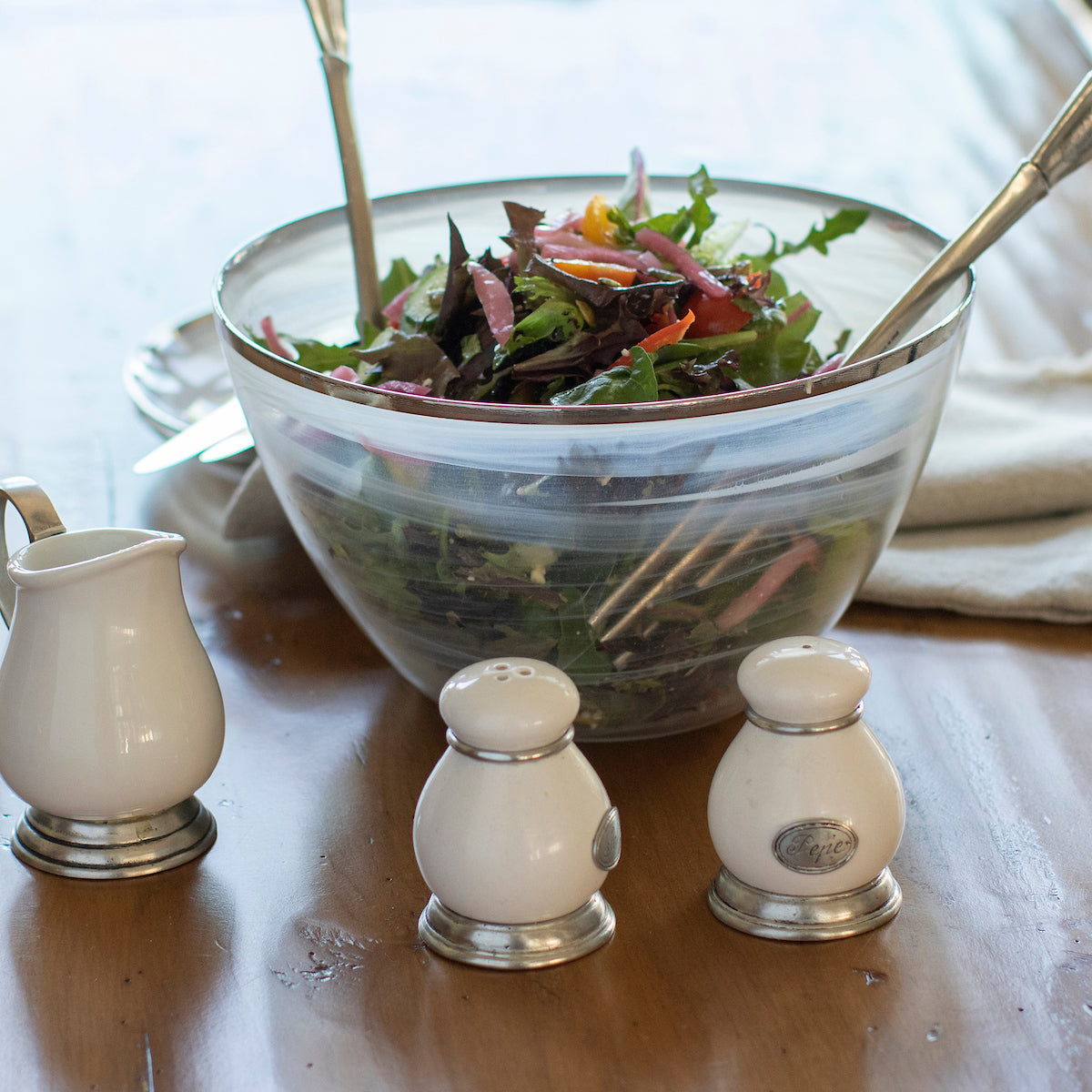 Tuscan ceramic salt and pepper set on a wood table in front of a salad