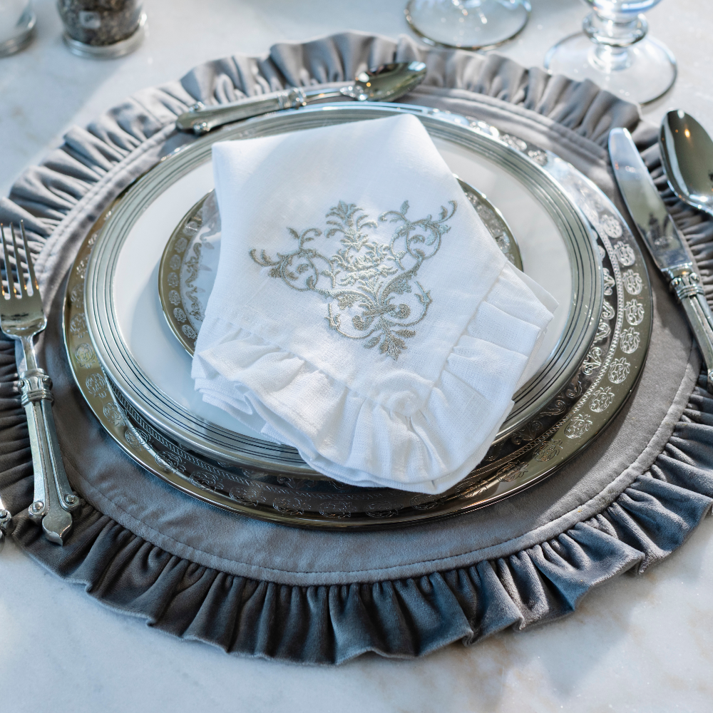 Elegant place setting with Vetro Platinum plates on a light blue velvet placemat with a white linen Snowflake Lane towel folded on it