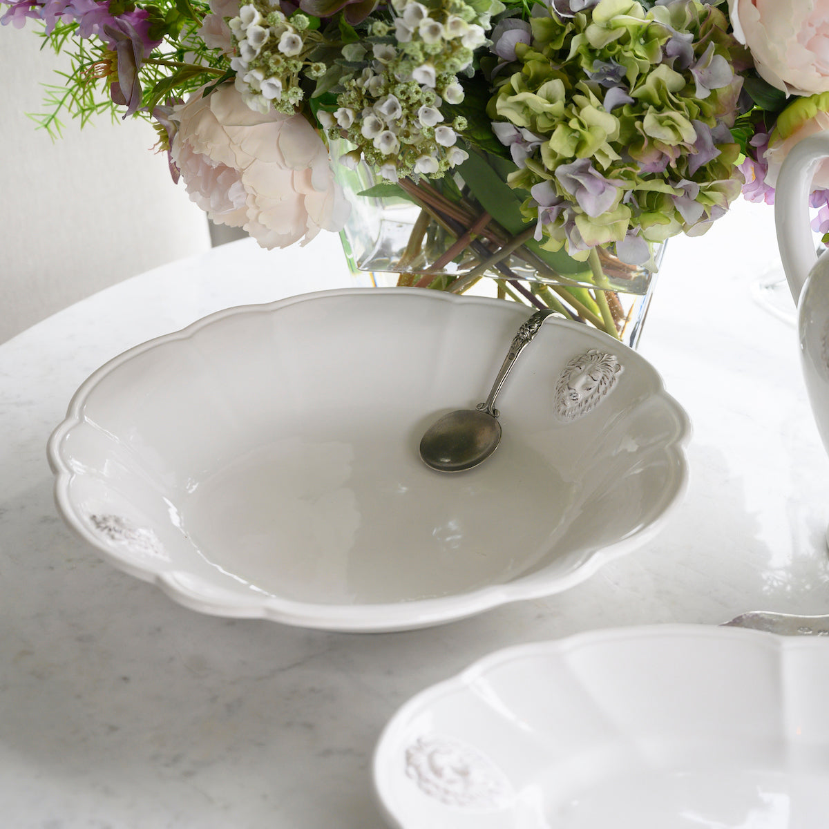 Arte Italica Renaissance Leone Serving Bowl White Handmade Italian Ceramic Lion Motif Large Table Bowl with spoon and flowers on counter