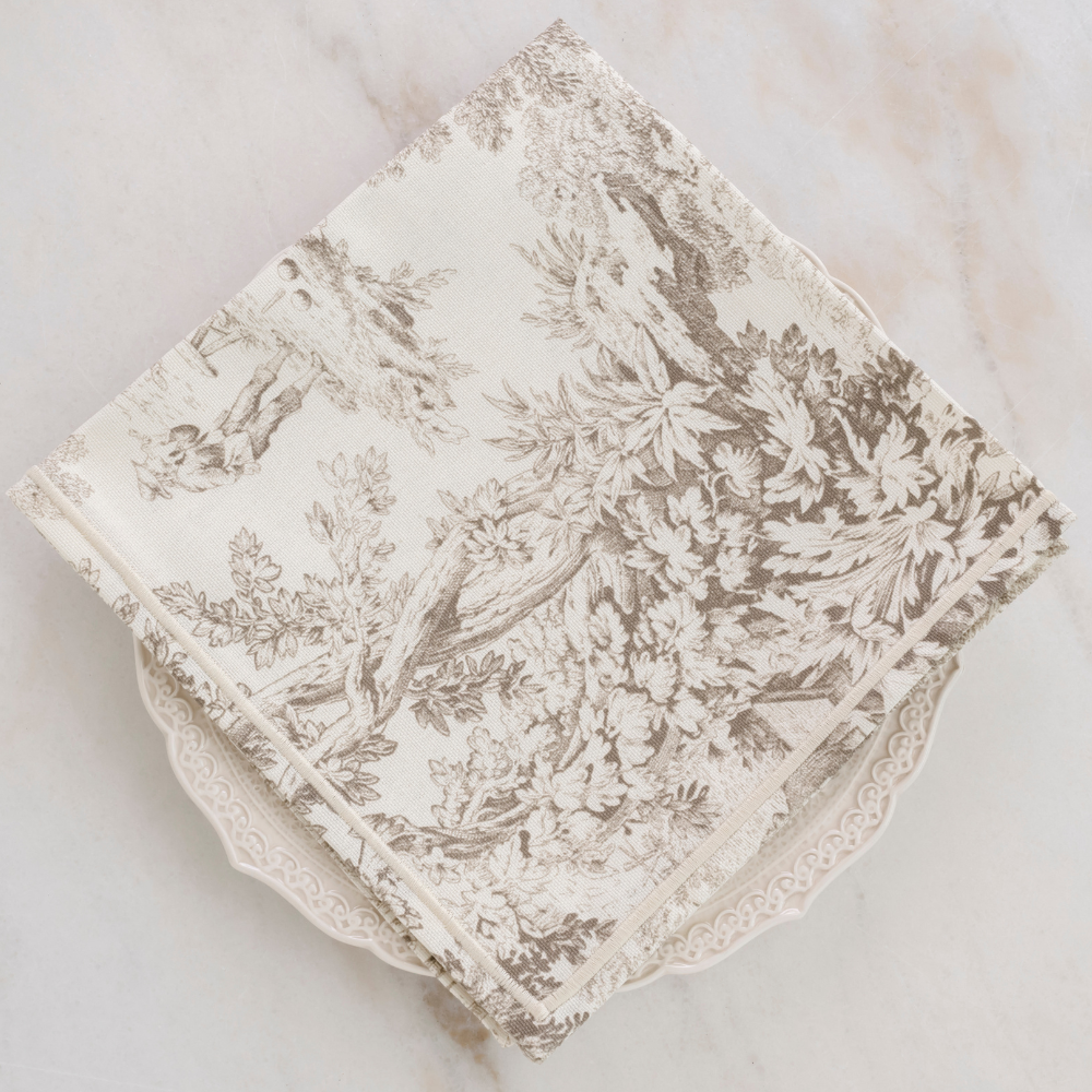 Montefalco Italian Toile Cotton Napkin in Latte and cream sitting on a plate on a marble background.