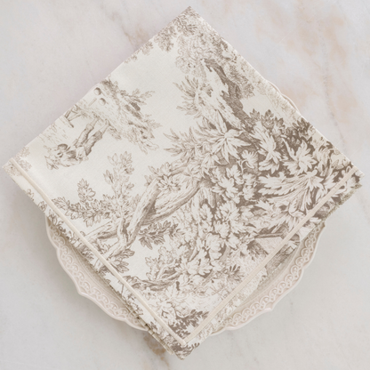 Montefalco Italian Toile Cotton Napkin in Latte and cream sitting on a plate on a marble background.