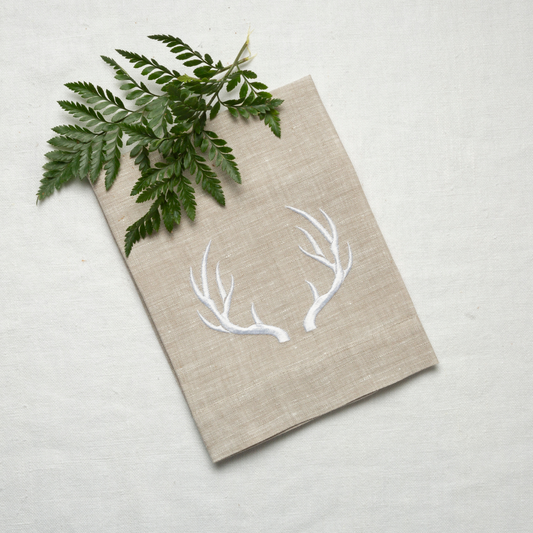 Antler Linen Tri-Fold Napkin next to green fern on white tablecloth