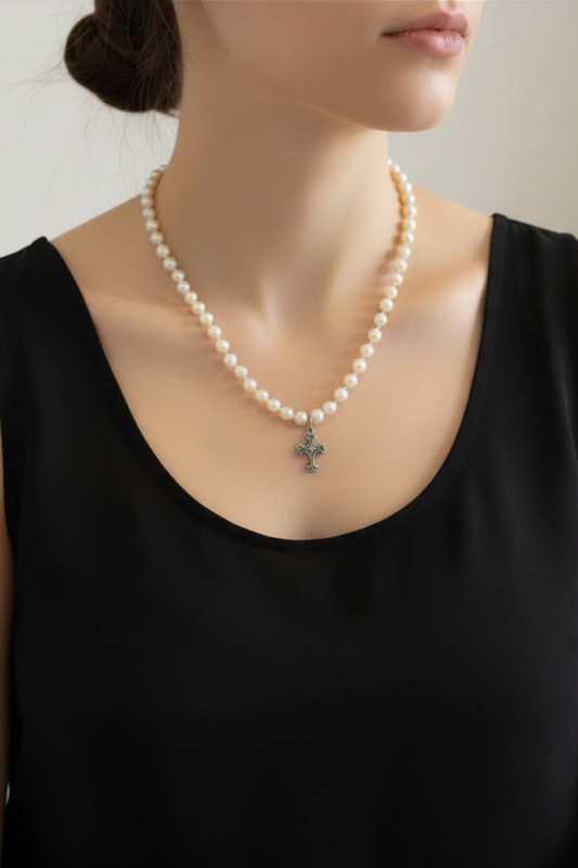 Pearl necklace with a cross pendant worn by a person in a black top.