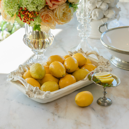 Antico Toscana ceramic rectangular dish with vine detail on the rim filled with lemons on a white table with flowers and pewter pedestal dish