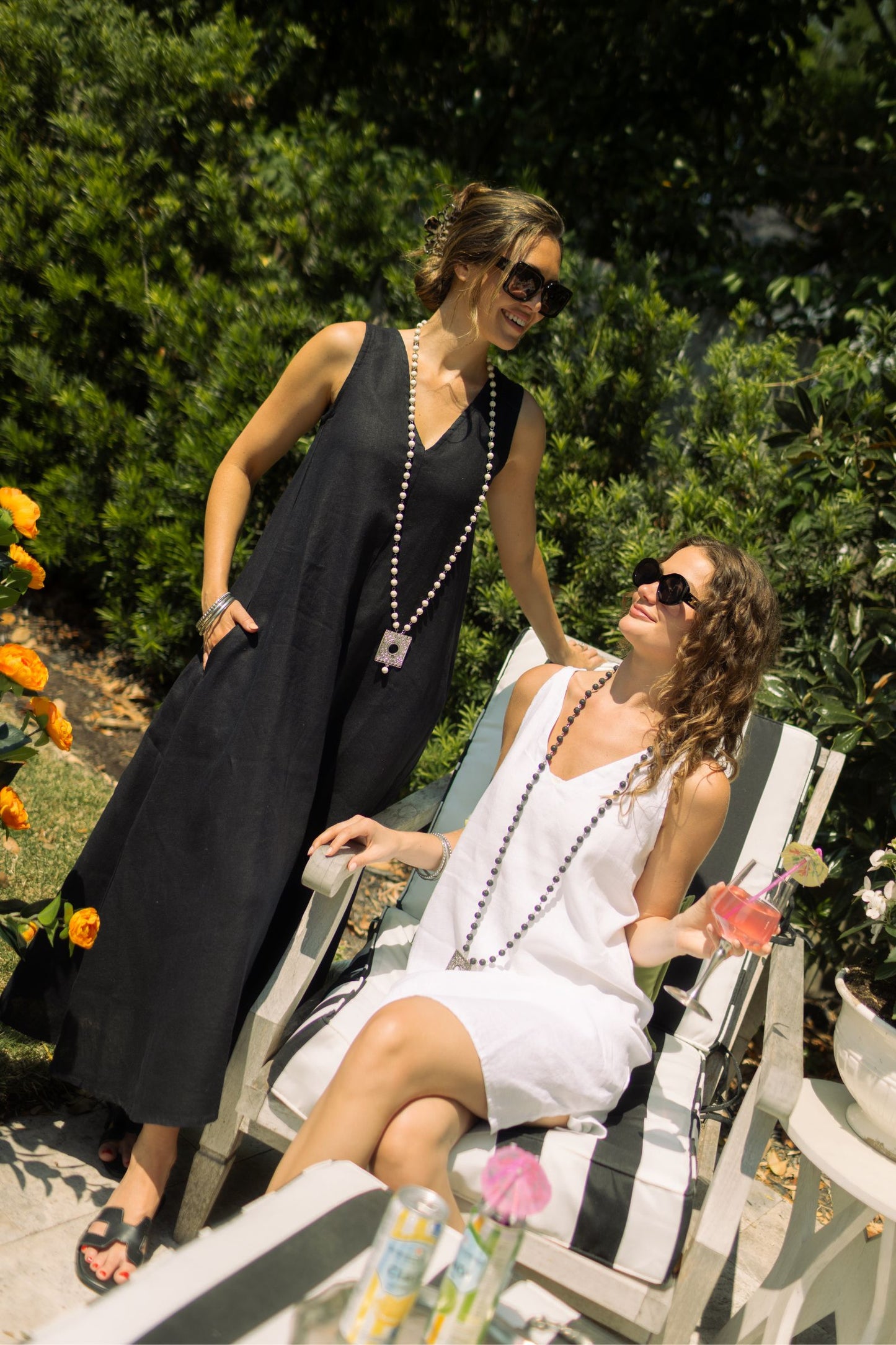 Two women posing outdoors, one wearing black linen Katherine dress paired with Boho necklace. --Arte Italica and Crown Linen Designs