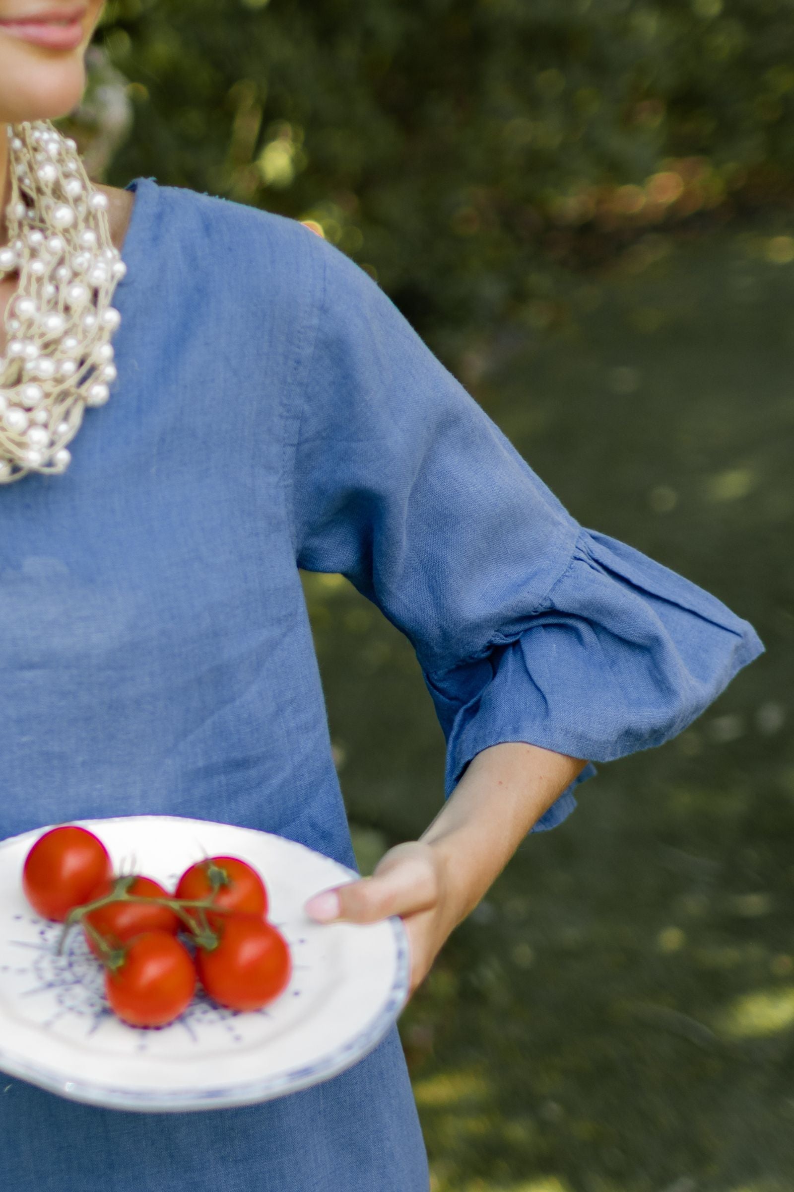 Detailed shot of ruffle bell sleeve of blue linen Bethany dress on model posing outdoors. --Arte Italica and Crown Linen Designs