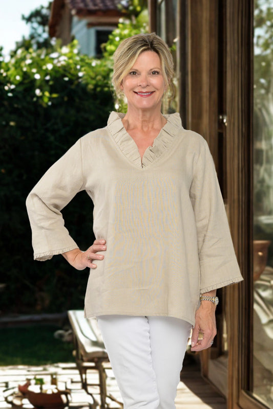 Woman wearing a beige blouse and white pants standing outdoors.