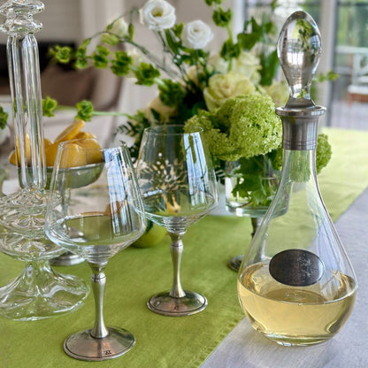 Glass decanter with pewter accents and Sienna wine glasses on a table with flowers and fruit