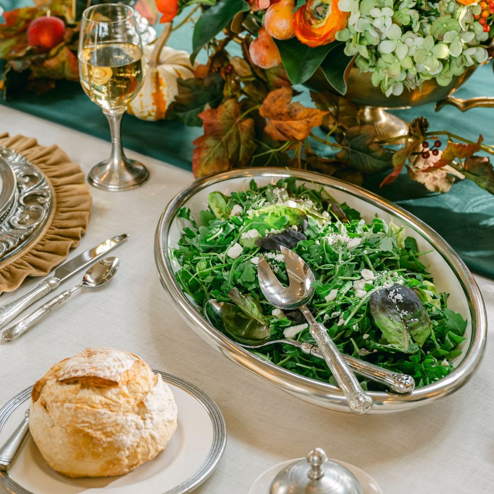 Decorative table setting with a salad in a Tuscan oval platter, bread, and wine glasses.