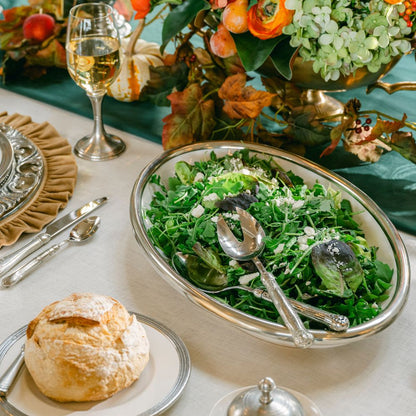 Decorative table setting with a salad in a Tuscan oval platter, bread, and wine glasses.
