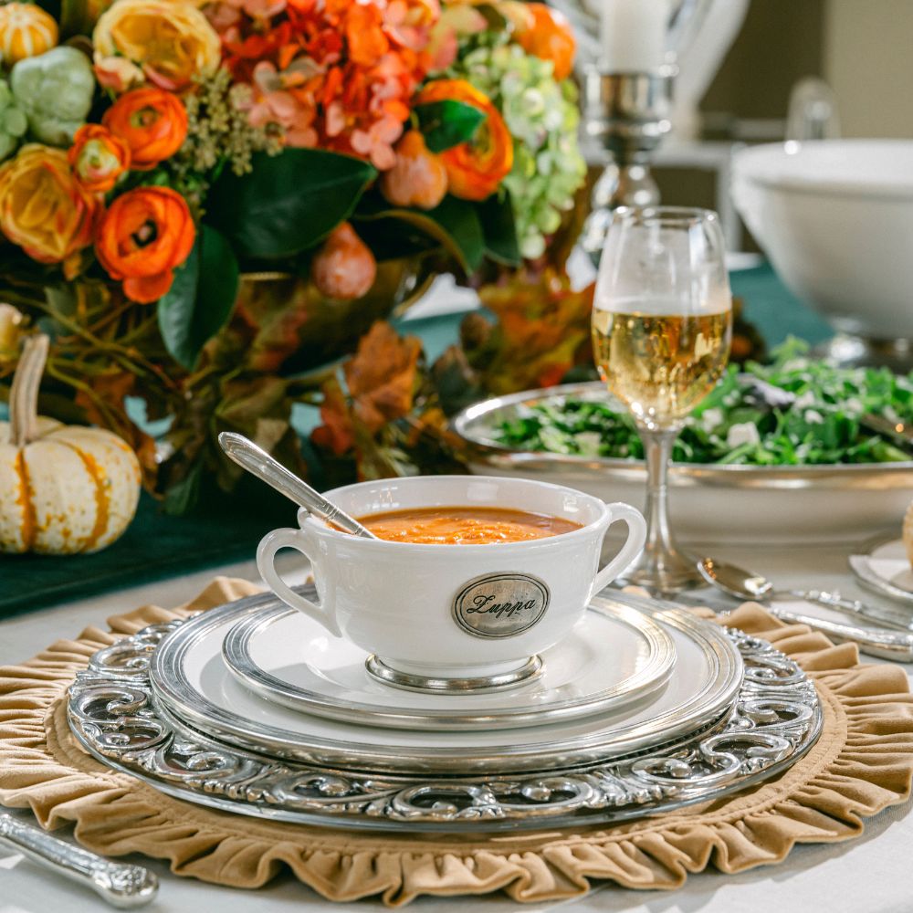 Decorative fall  table setting with a bowl of soup, wine glass, and floral arrangement.