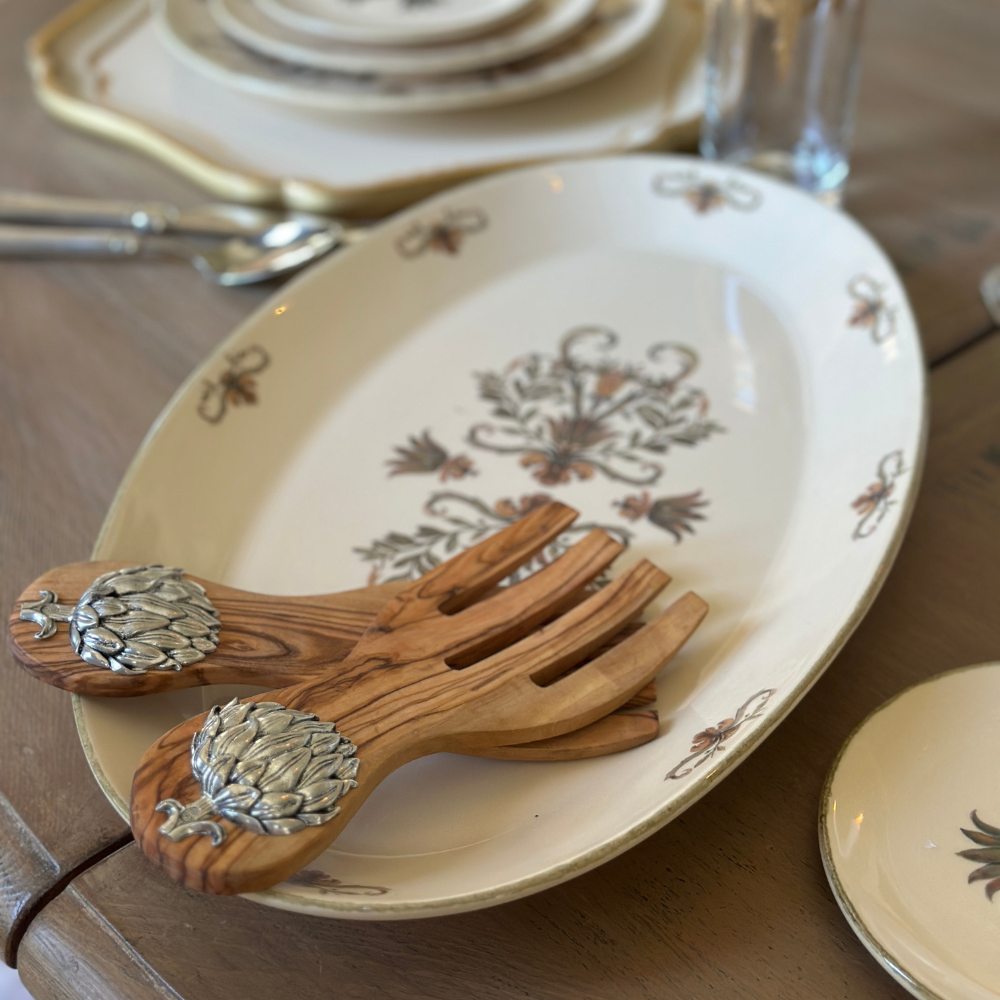 Wooden salad servers with decorative handles on a patterned ceramic plate.