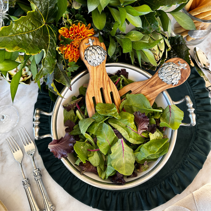 Bowl of salad with wooden spoons on a decorative table setting with flowers and cutlery.