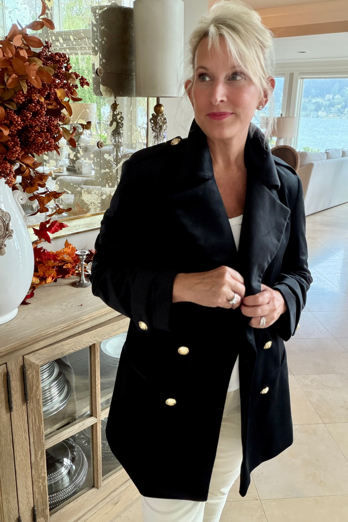 Woman wearing the Crown Linen Avery Luxury Velvet Blazer in black with gold buttons, styled with white trousers in an elegantly decorated fall interior with autumn floral arrangement