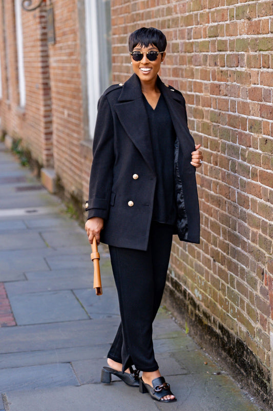 Woman in a black outfit with an Avery Wool Blend coat standing against a brick wall