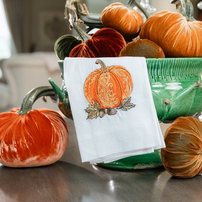 A baroque embroidered pumpkin in orange on a white linen towel on a Scavo Harvest green footed bowl with velvet pumpkins on a table