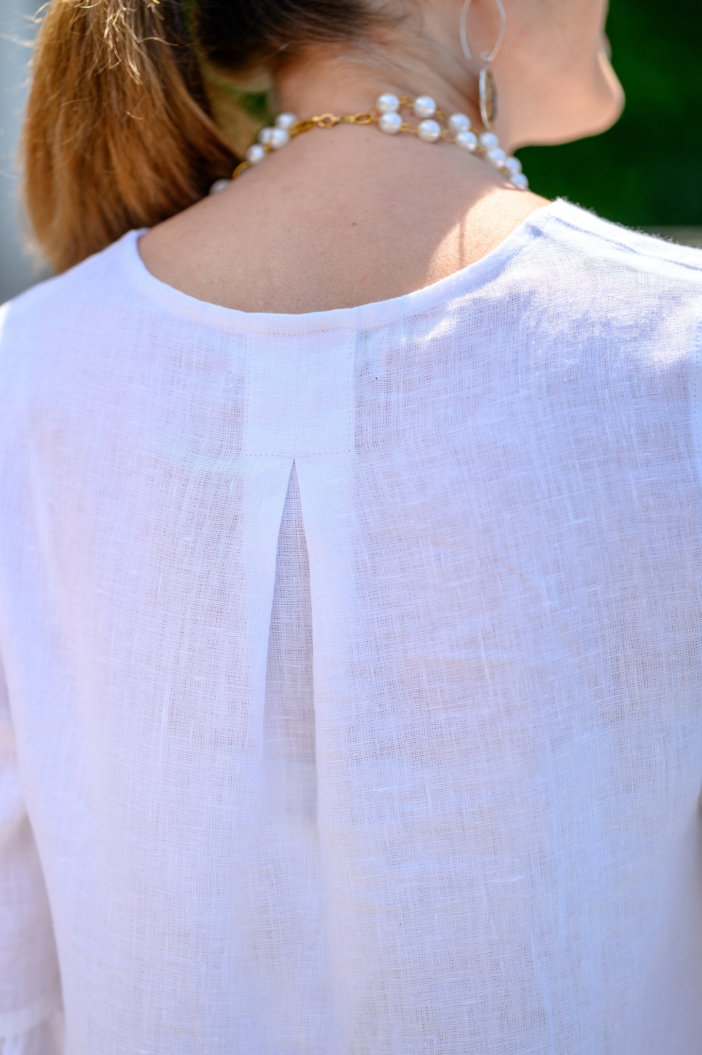 Back detail of top in white linen with model posing outside. --Arte Italica and Crown Linen Designs