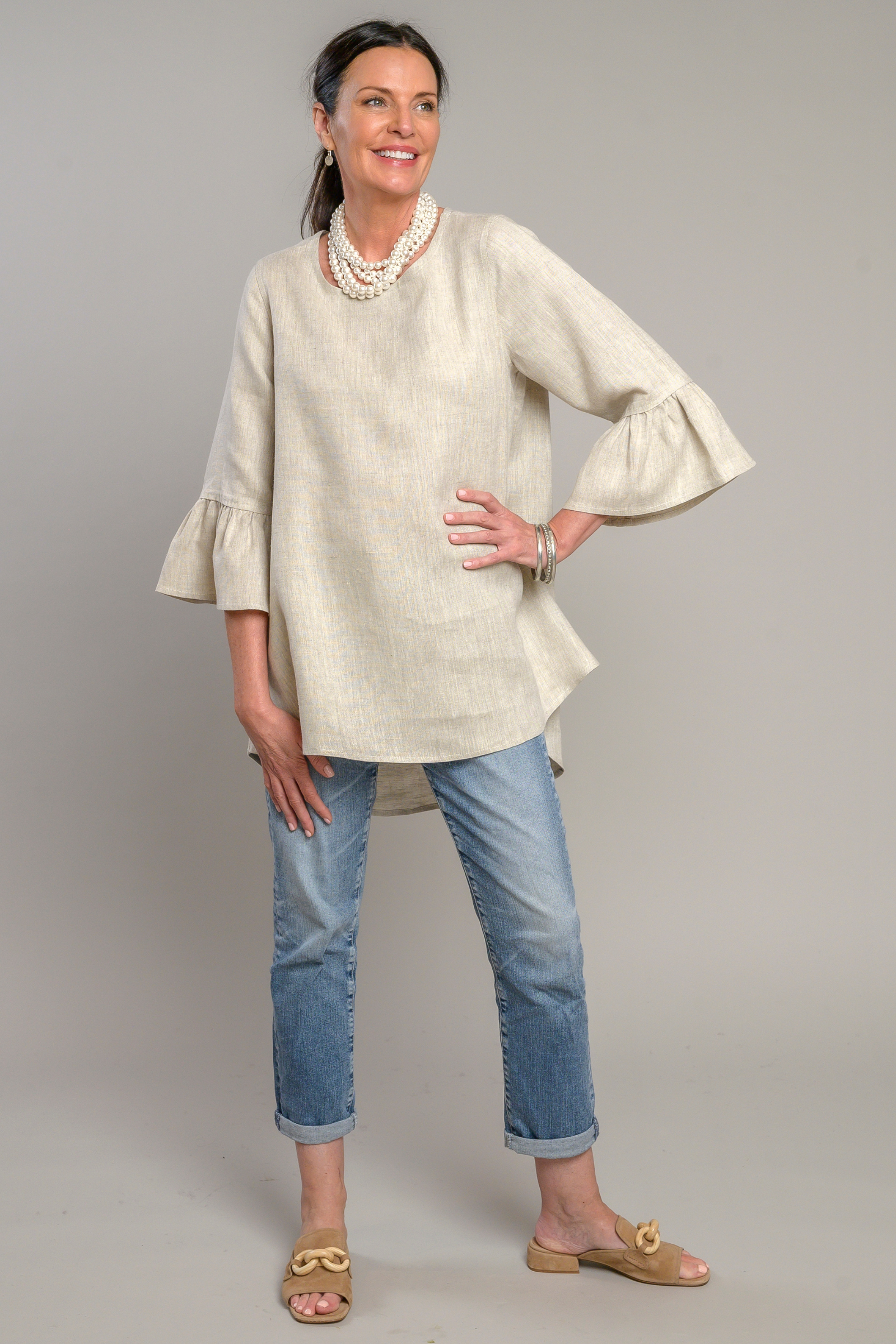 Woman wearing a soft flax colored Bella linen top with 3/4 bell sleeves and jeans with a stacked pearl necklace and pewter bangles. --Arte Italica and Crown Linen Designs