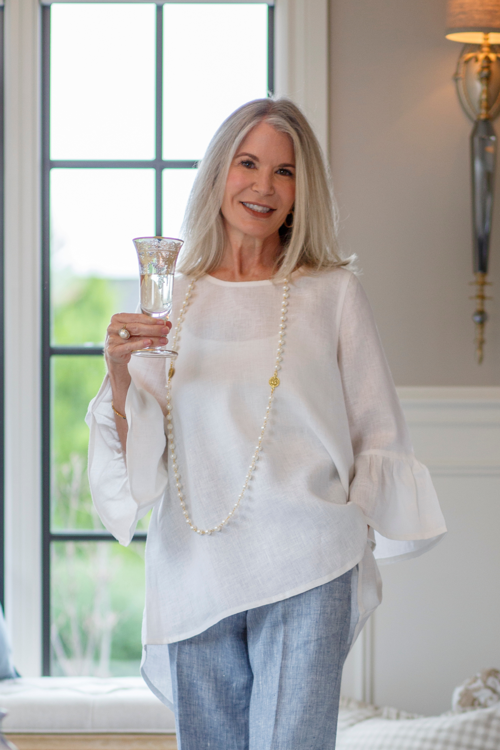 Woman wearing a Bella Bell sleeve top in White Summer weight linen holding a glass by a window