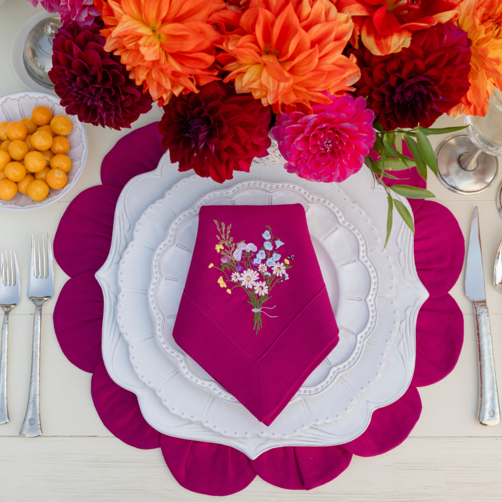 Bella Bianca Ceramic dishes on a Magenta Linen Petal Placemat with a Wildflower bouquet embroidered napkin folded on top 