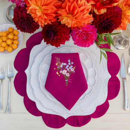 Bella Bianca Ceramic dishes on a Magenta Linen Petal Placemat with a Wildflower bouquet embroidered napkin folded on top 