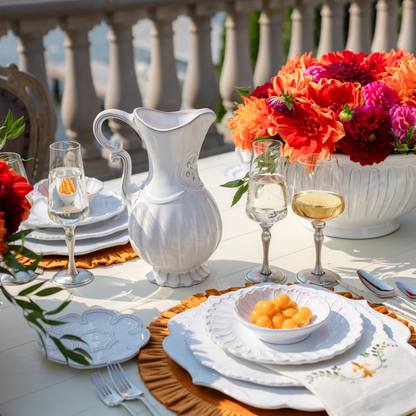 An outdoor table set with Bella Bianca placesetting with a Garden urn with dahlias and a pitcher