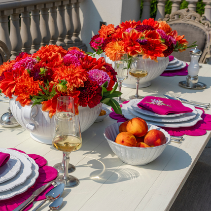 An outdoor table set with Bella Biana dishes and wine with peaches in a small serving bowl and two bright centerpieces of orange and magenta dahlias