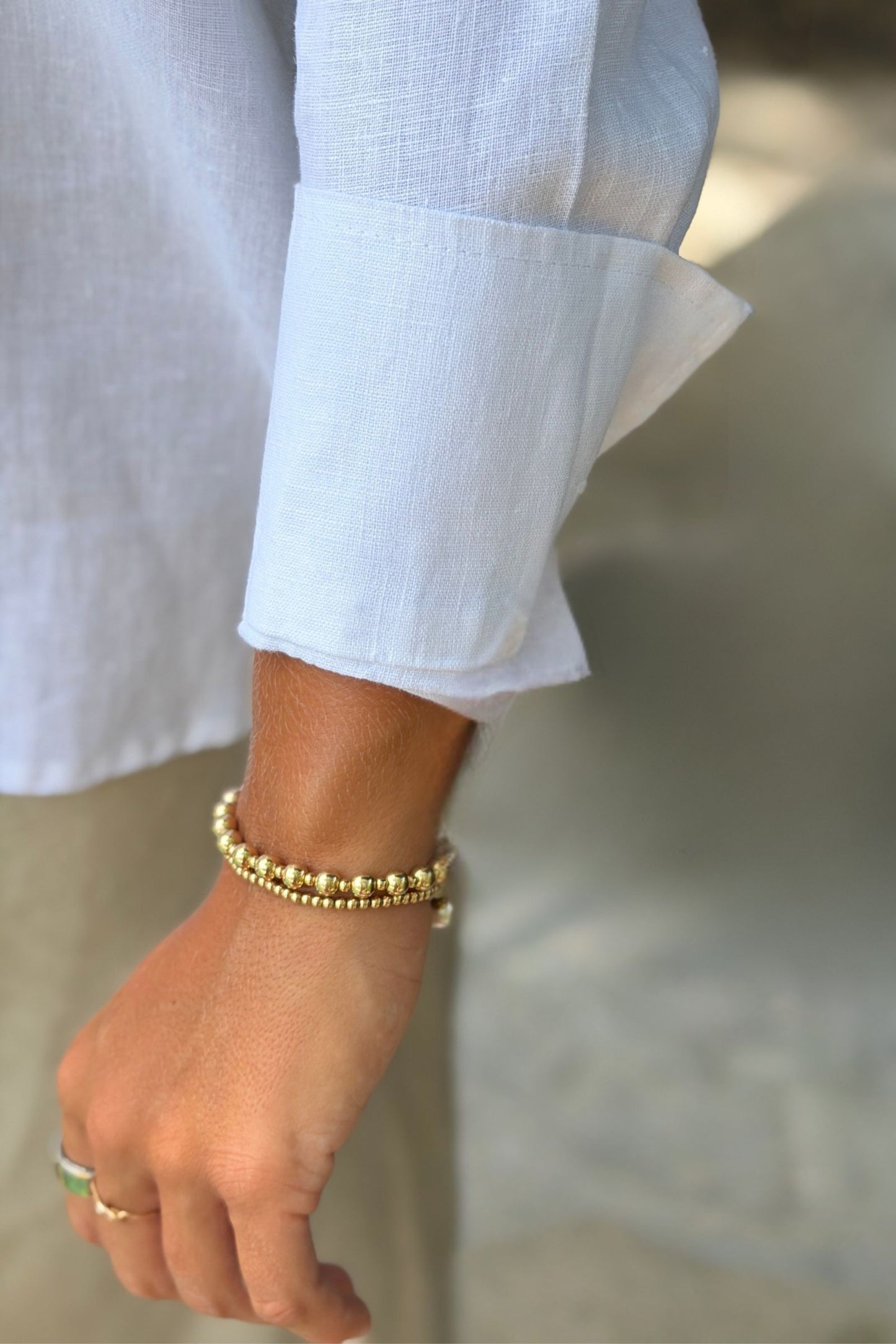 A close-up of the sleeve cuff on a white linen Belmont blouse shirt, showing the person's wrist with gold bracelets.