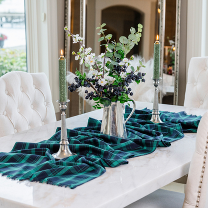 Black watch tartan runner on a white marble table with two Alaria pewter candlesticks and a pewter pitcher with greens and berries