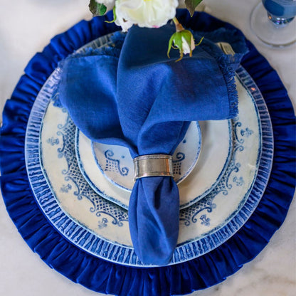 Blue napkin folded on a Burano ceramic plate with a white flower, set against a blue placemat.