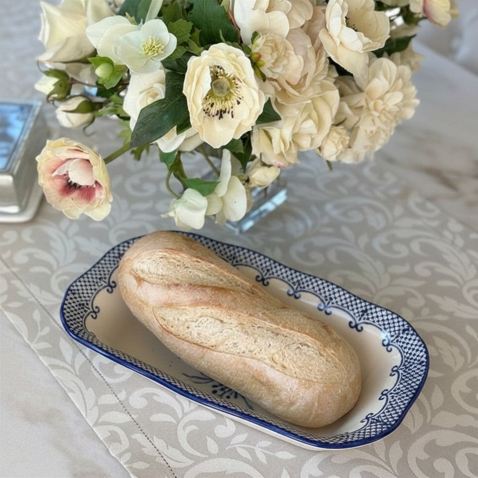 Loaf of bread on a Burano Blue Rectangular Dish holding a loaf of bread with a vase of flowers in the background