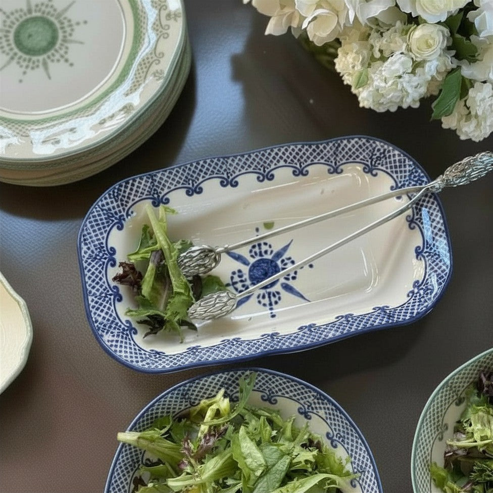 Blue and white Burano Rectangular Dish with salad and artichoke pewter tongs on a table with flowers.