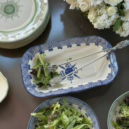 Blue and white Burano Rectangular Dish with salad and artichoke pewter tongs on a table with flowers.