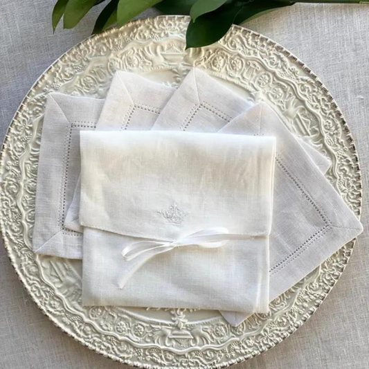 White hemstitched linen cocktail napkins with a storage pouch detailed with a bow. Styled on a silver platter.