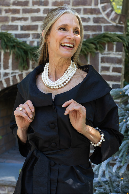 Close up of the Carment wide collared taffeta jacket with fabric covered buttons on a woman wearing pearls outside by a fireplace