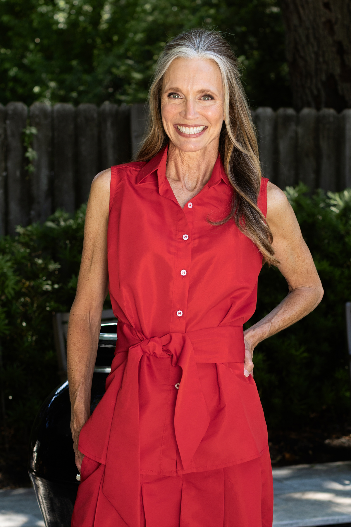 Woman standing outside wearing a red taffeta Caroline Sleeveless top