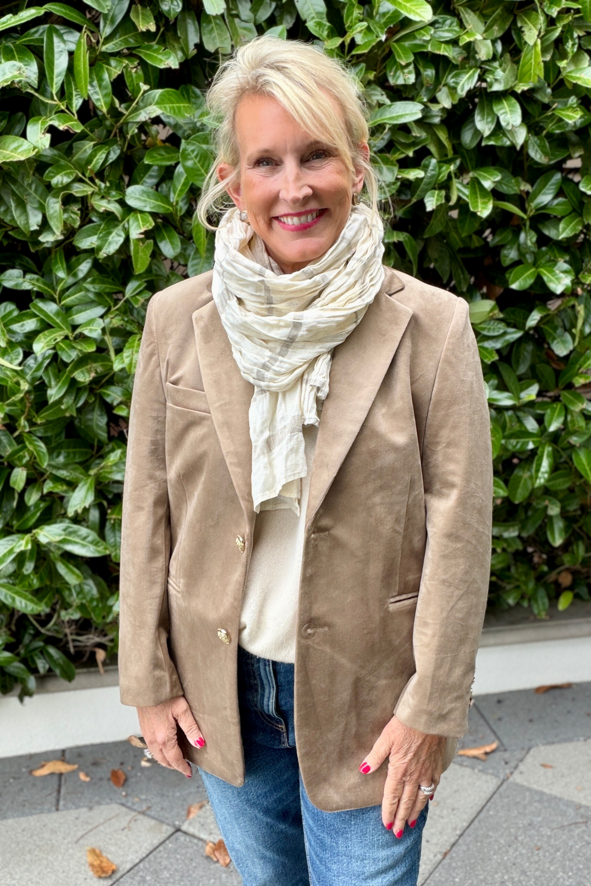 Charlie Velvet Blazer in mocha with gold buttons, styled with a striped scarf and jeans against a lush green hedge backdrop